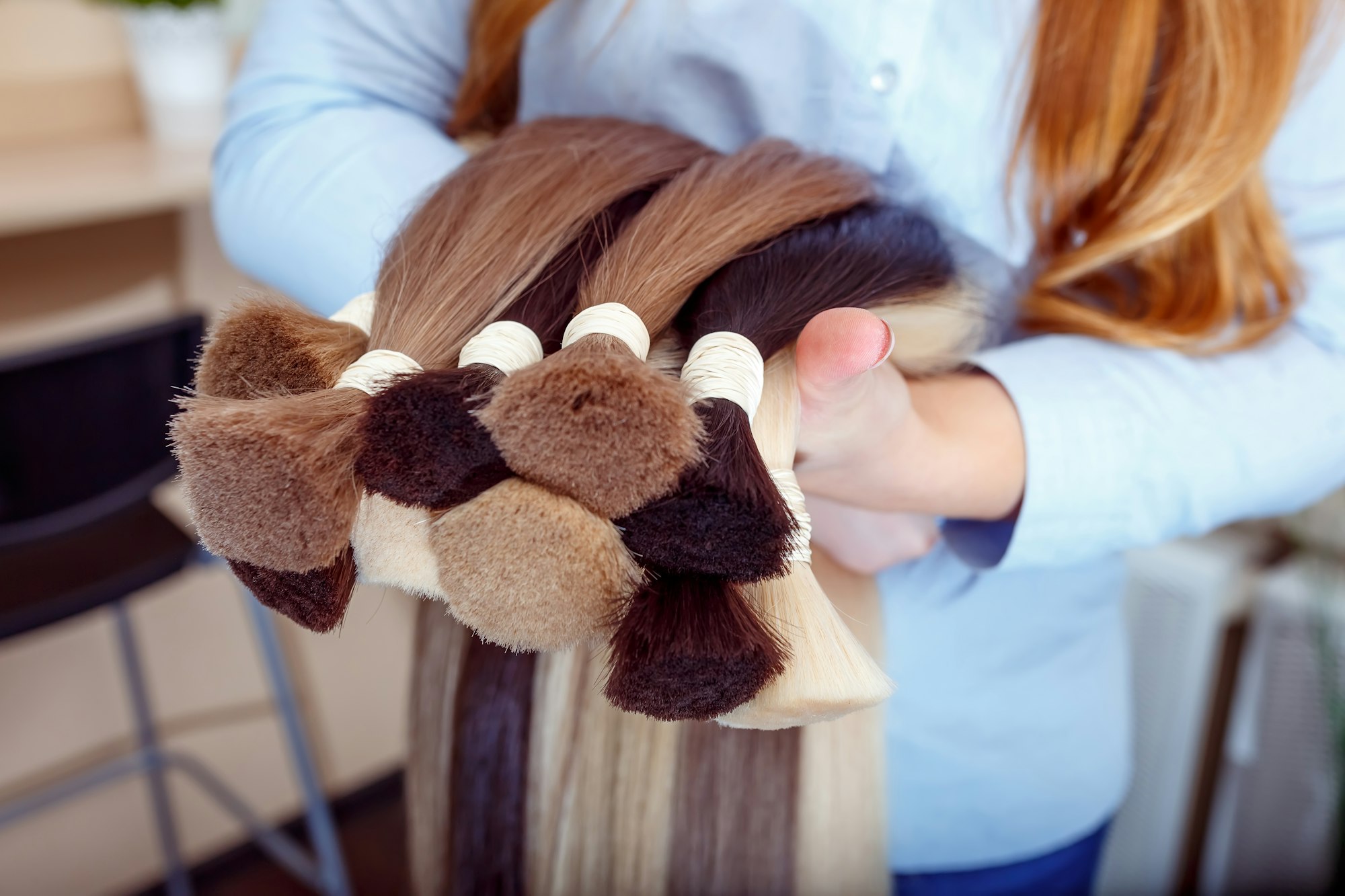 Woman holds hair extension equipment of natural hair. hair samples of different colors